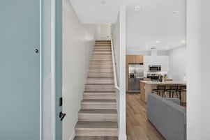 Una cucina moderna con isola centrale, elettrodomestici in acciaio inossidabile e un divano grigio in un ambiente luminoso e aperto.