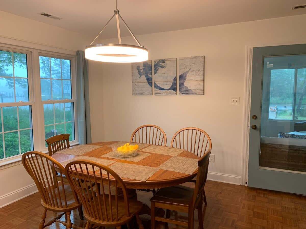 A dining area with a round table, six wooden chairs, a central light fixture, and a door with a view.