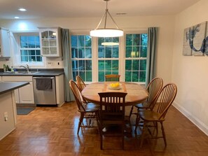 A dining area with a round wooden table and chairs, a kitchen with a window, and a pendant light. - Sirena's Isle Waterfront
boat lift, pet friendly (Oriental)