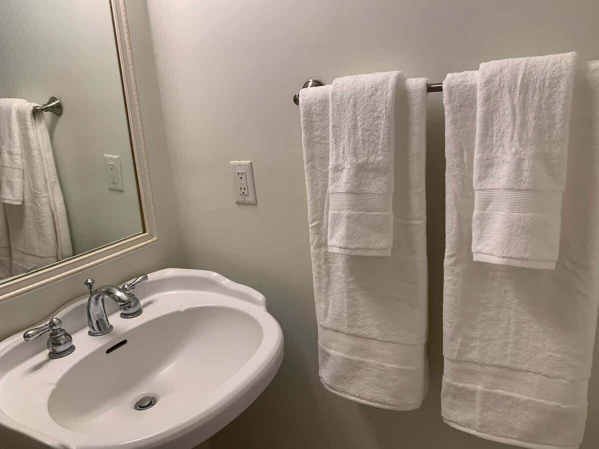 A bathroom with a white sink, two faucets, and a mirror. There are two white towels hanging on a towel rack.