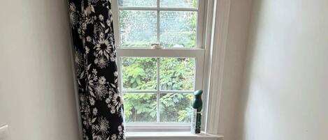 A small bathroom with a toilet, a window with a view of greenery, a shower curtain, and a toilet paper holder.