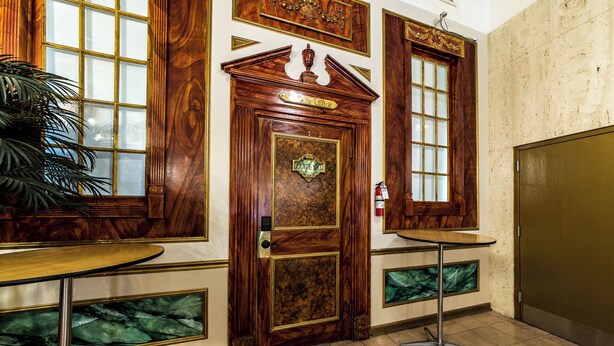 Une pièce avec une porte en bois portant l’inscription « Suite 100 », une petite table, une plante en pot et un extincteur.