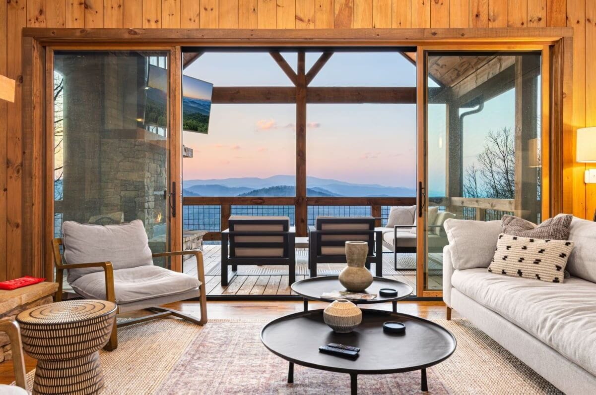 A wooden interior with a sofa, chairs, a coffee table, and a view of mountains through large glass doors.