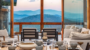 Un comedor con una mesa dispuesta para dos, un sofá y vistas a la montaña a través de ventanas amplias.