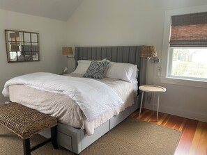 Quarto com cama grande, mesas de cabeceira, um banco, espelho e janela com persianas.