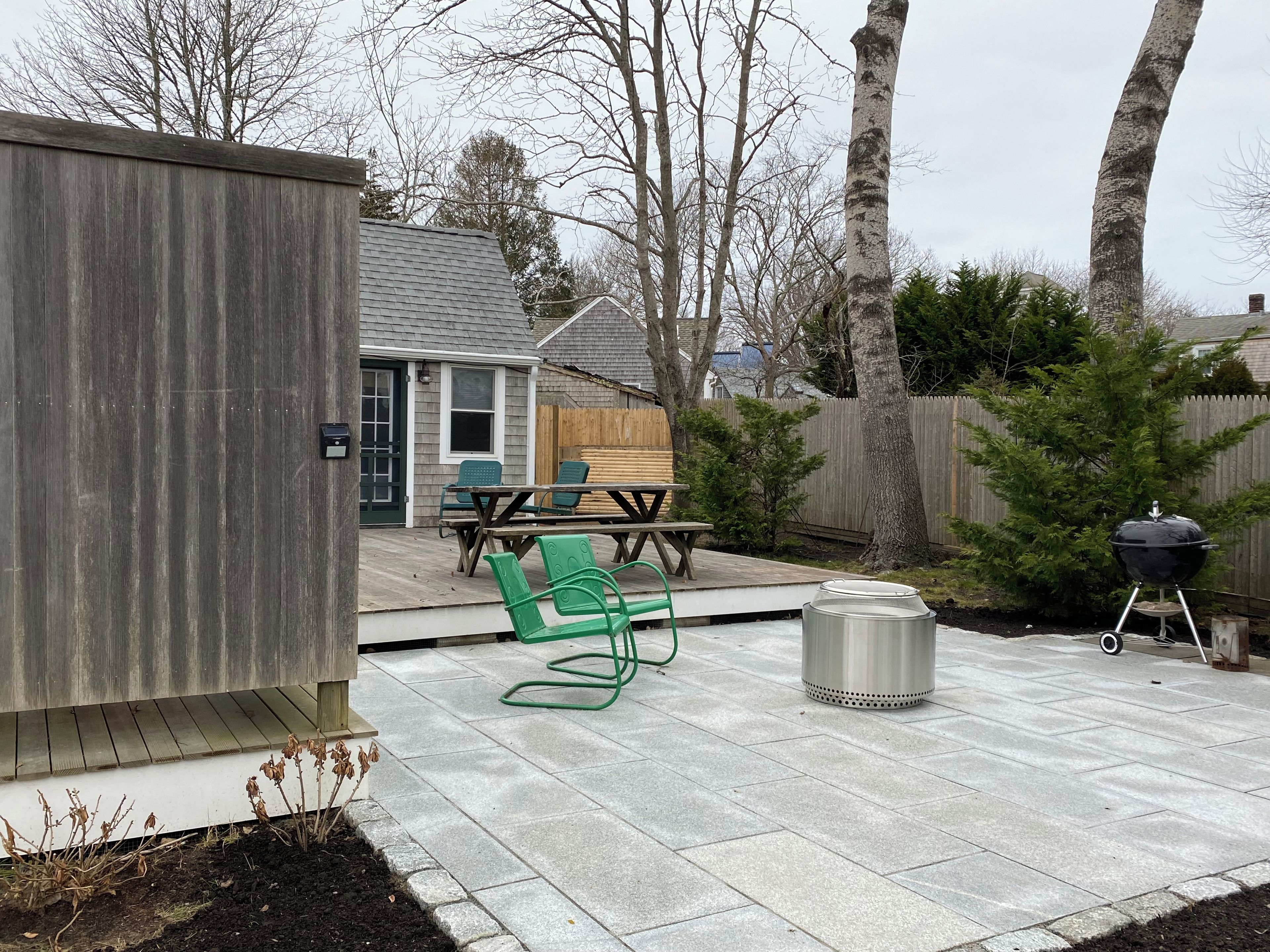 Un jardin avec une terrasse, un barbecue et une plateforme en bois.