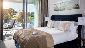 Ett hotellrum med en säng, utsikt över en parkeringsplats, en stol och en tavla på väggen.