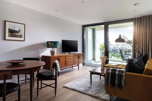 Ein modernes Wohnzimmer mit Essbereich, einem Flachbildfernseher und einem großen Fenster mit Blick auf die Stadt.