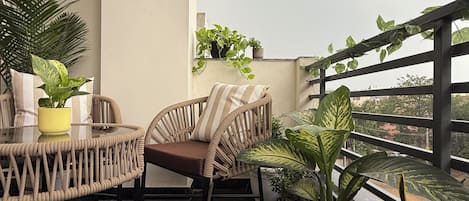 Uma varanda com cadeira de vime, uma mesa pequena e plantas em vasos.