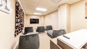 Une salle de conférence équipée d’un téléviseur à écran plat, de chaises grises rembourrées, d’une table blanche et d’une télécommande posée sur la table.
