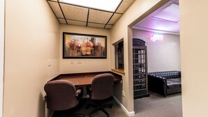 Une pièce comprenant un bureau, deux chaises, un tableau, un néon, une bibliothèque et un canapé en cuir.