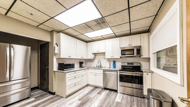 Une cuisine moderne dotée d’appareils électroménagers en acier inoxydable, de meubles blancs et d’un parquet en bois disposé en motif chevrons.