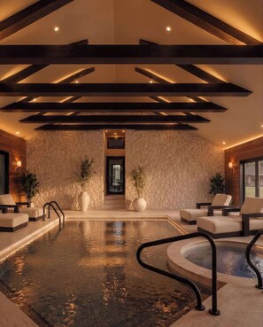 An indoor swimming pool with a stone wall and wooden beams, surrounded by lounge chairs and a staircase leading to an upper level. - Fauzan, a Private Residential Resort (Wall Township)