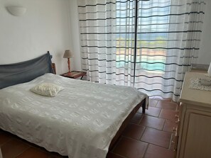 A bedroom with a bed, a nightstand, a lamp, a window with curtains, and a dresser. - Beachfront Home (Bormes-les-Mimosas)