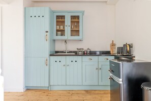 Una cocina con armarios azul claro, un refrigerador negro y piso de madera.