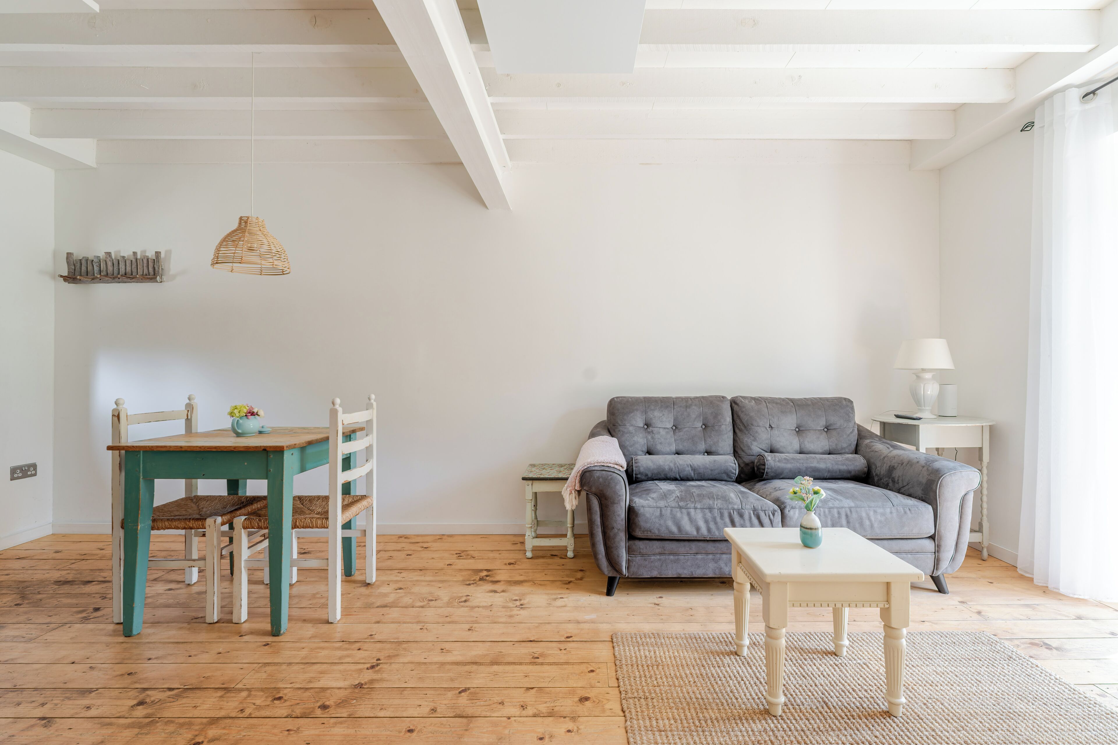 Un salon avec un canapé gris, une table à manger en bois avec des chaises, une petite table blanche et un luminaire suspendu.