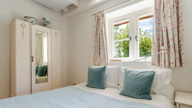 Un dormitorio con cama, armario, ventana con cortinas y mesita de noche.