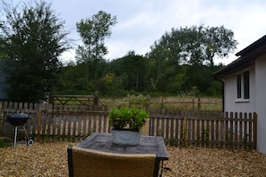 A patio with a wicker chair, a potted plant, a barbecue grill, and a wooden fence. - Lily of the Valley (Keynsham)