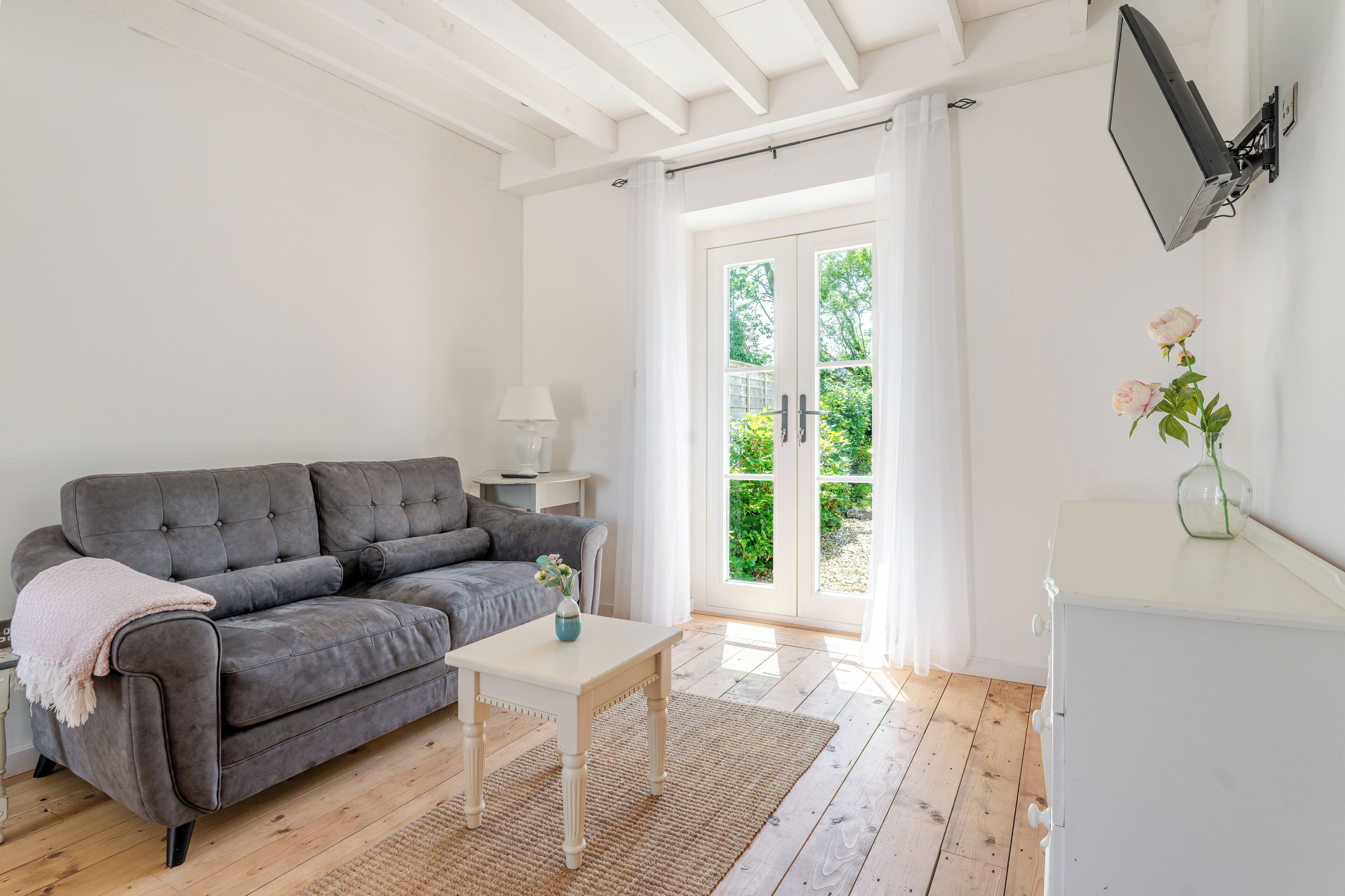 Una sala de estar con un sofá gris, una mesita blanca y un armario blanco.