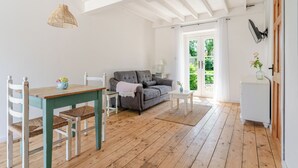 Una sala de estar con un sofá, una mesa de comedor con sillas, una lámpara colgante y vistas a través de un ventanal.