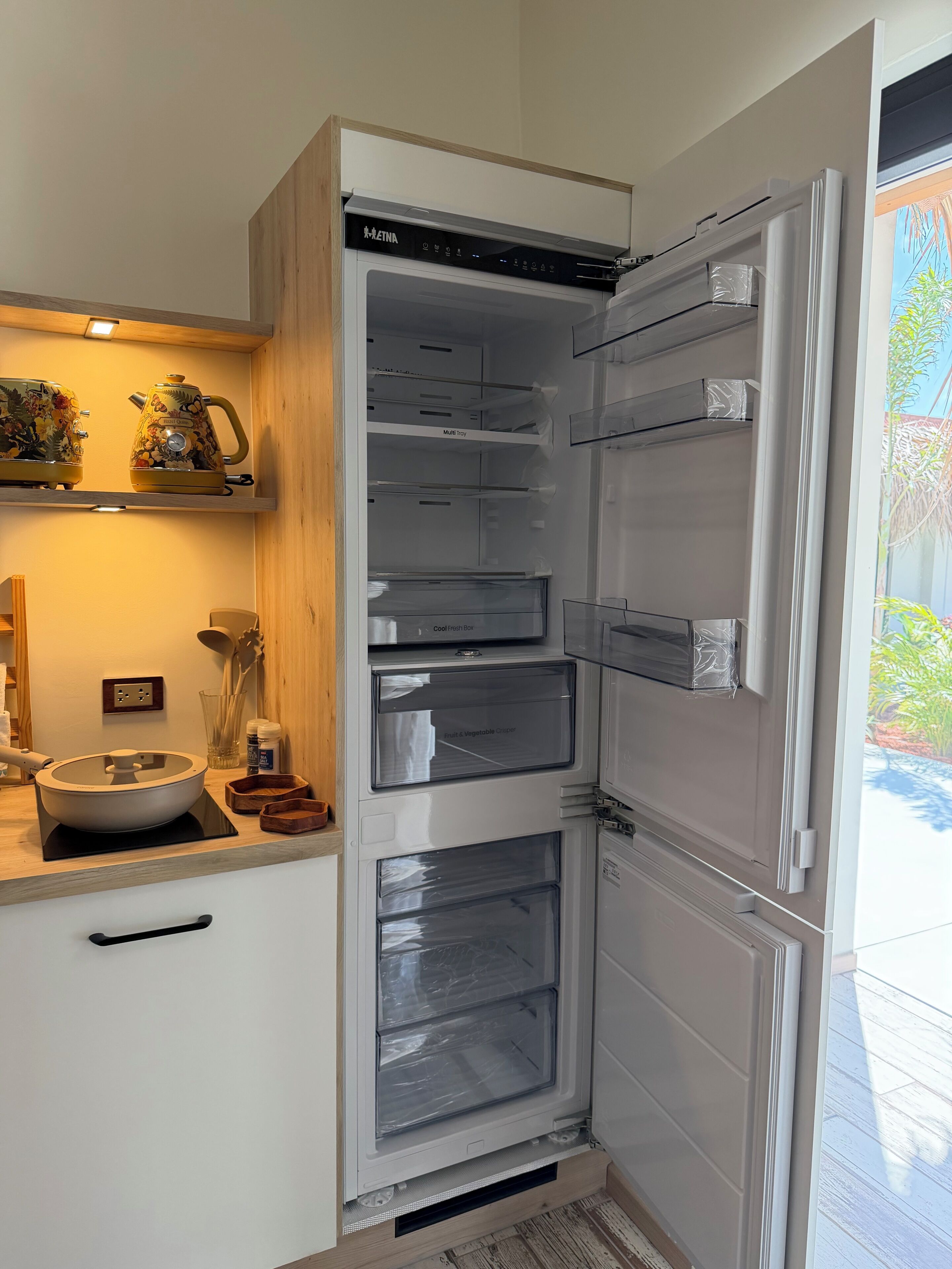 Une cuisine moderne dotée d’un réfrigérateur encastré, d’un meuble de rangement à plusieurs niveaux et d’un plan de travail avec un saladier et des ustensiles.