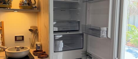 Une cuisine moderne dotée d’un réfrigérateur encastré, d’un meuble de rangement à plusieurs niveaux et d’un plan de travail avec un saladier et des ustensiles.