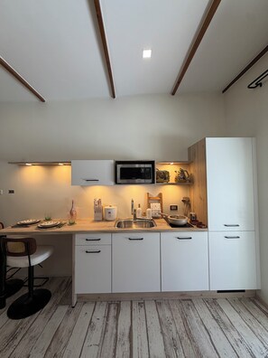 Une cuisine moderne avec des meubles blancs, un évier en acier inoxydable et un four à micro-ondes installé au-dessus.