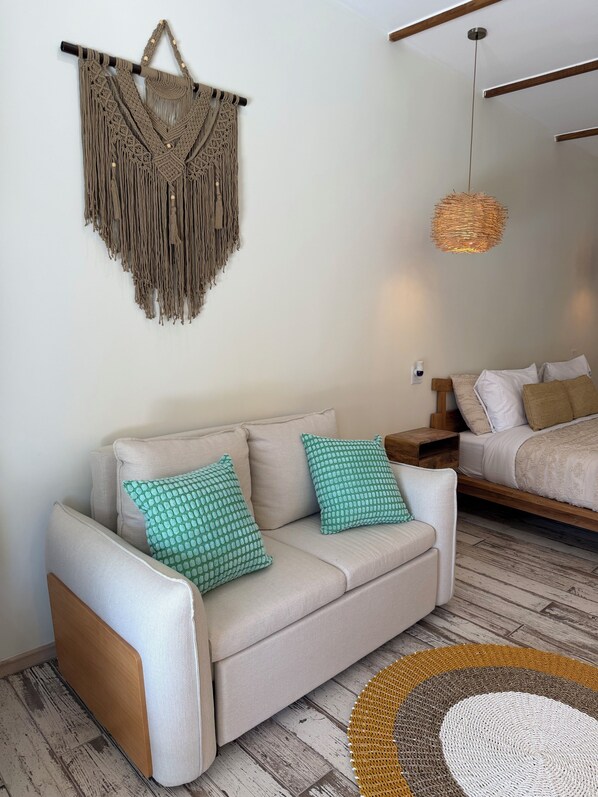 Un salon comprenant un canapé, deux coussins, une décoration murale en macramé, un luminaire tressé et un tapis rond tissé.