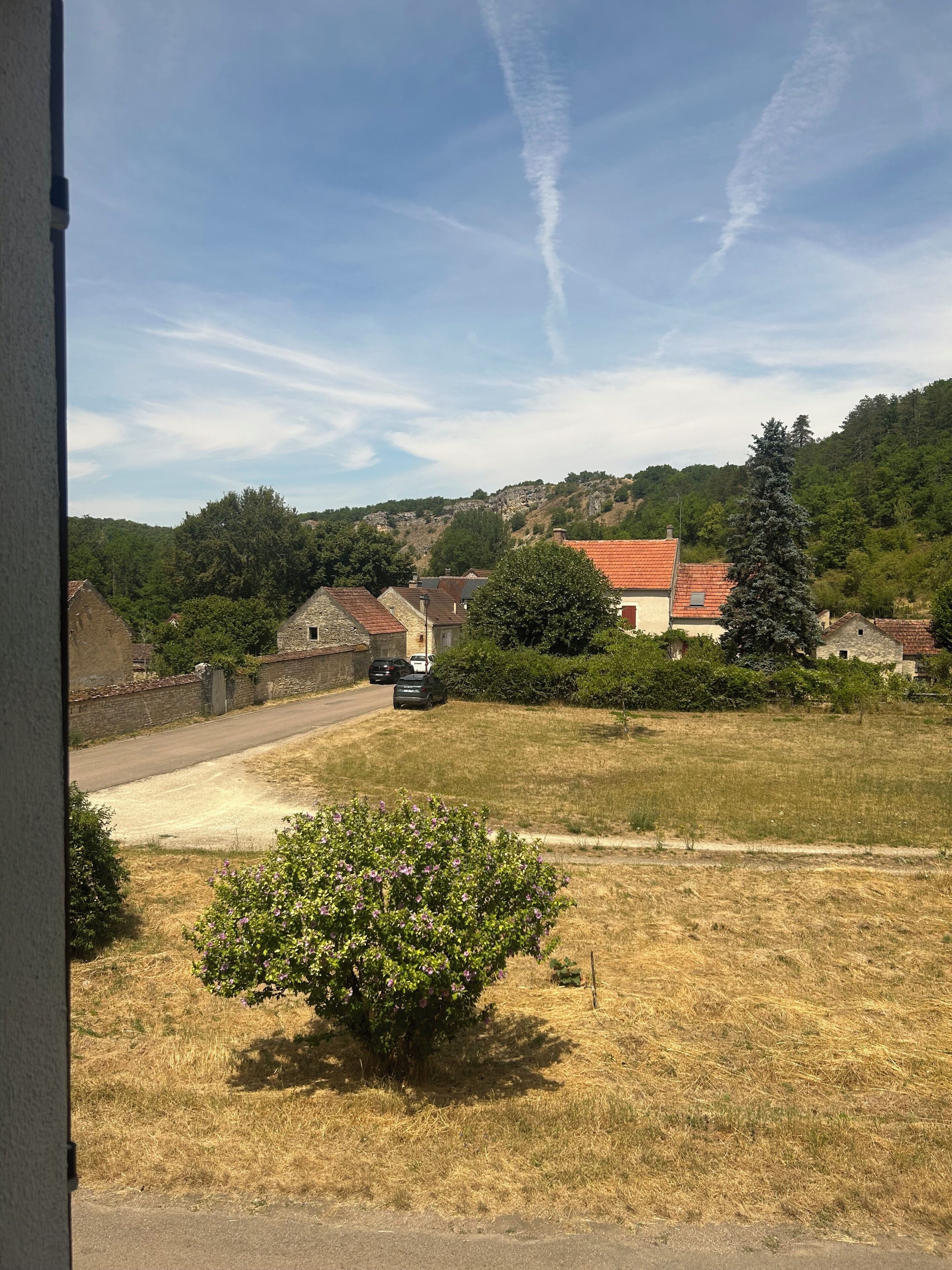 A rural landscape with a road, parked cars, and houses with red roofs.