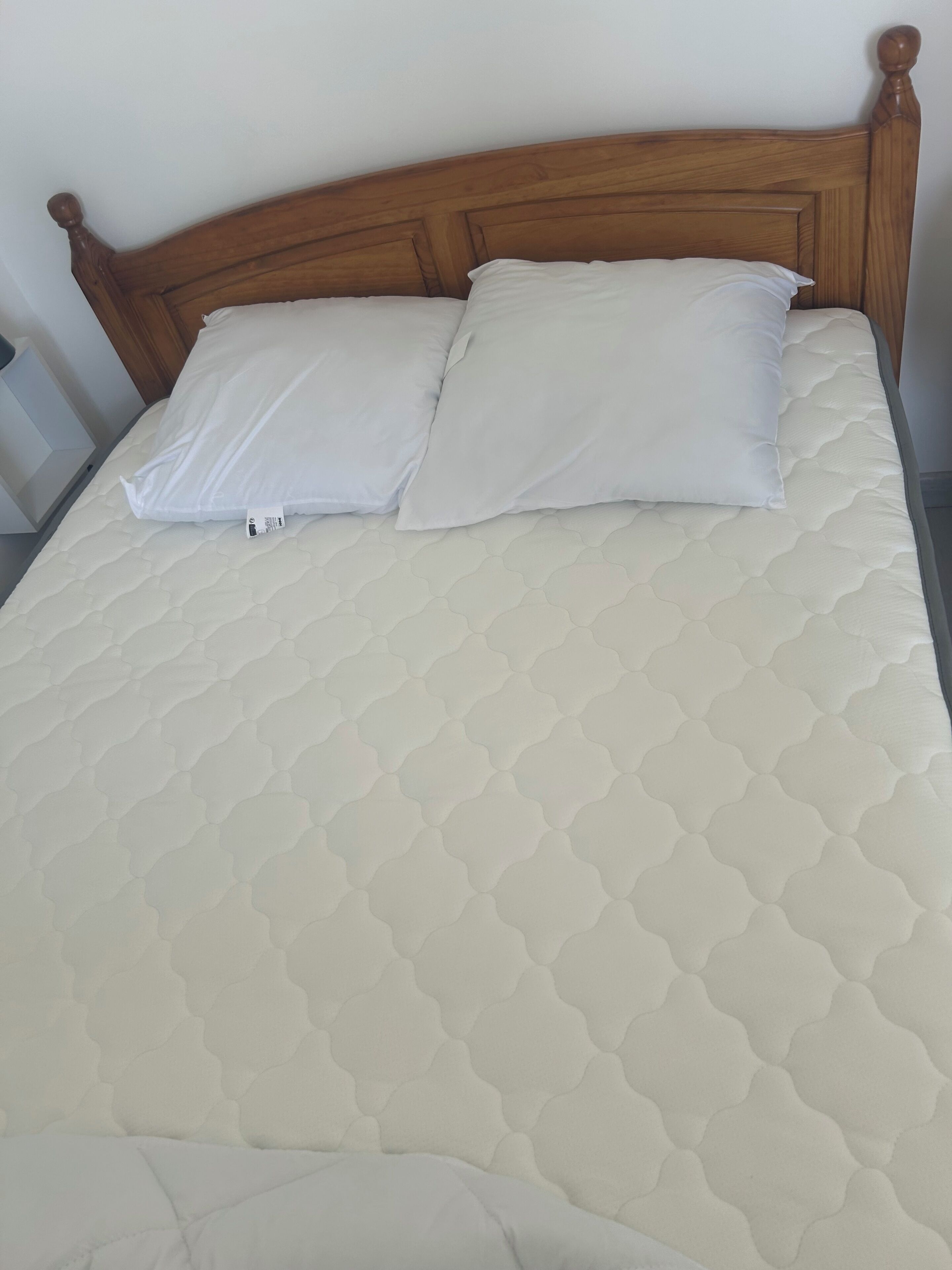 A bed with a wooden headboard, two pillows, and a quilted mattress.