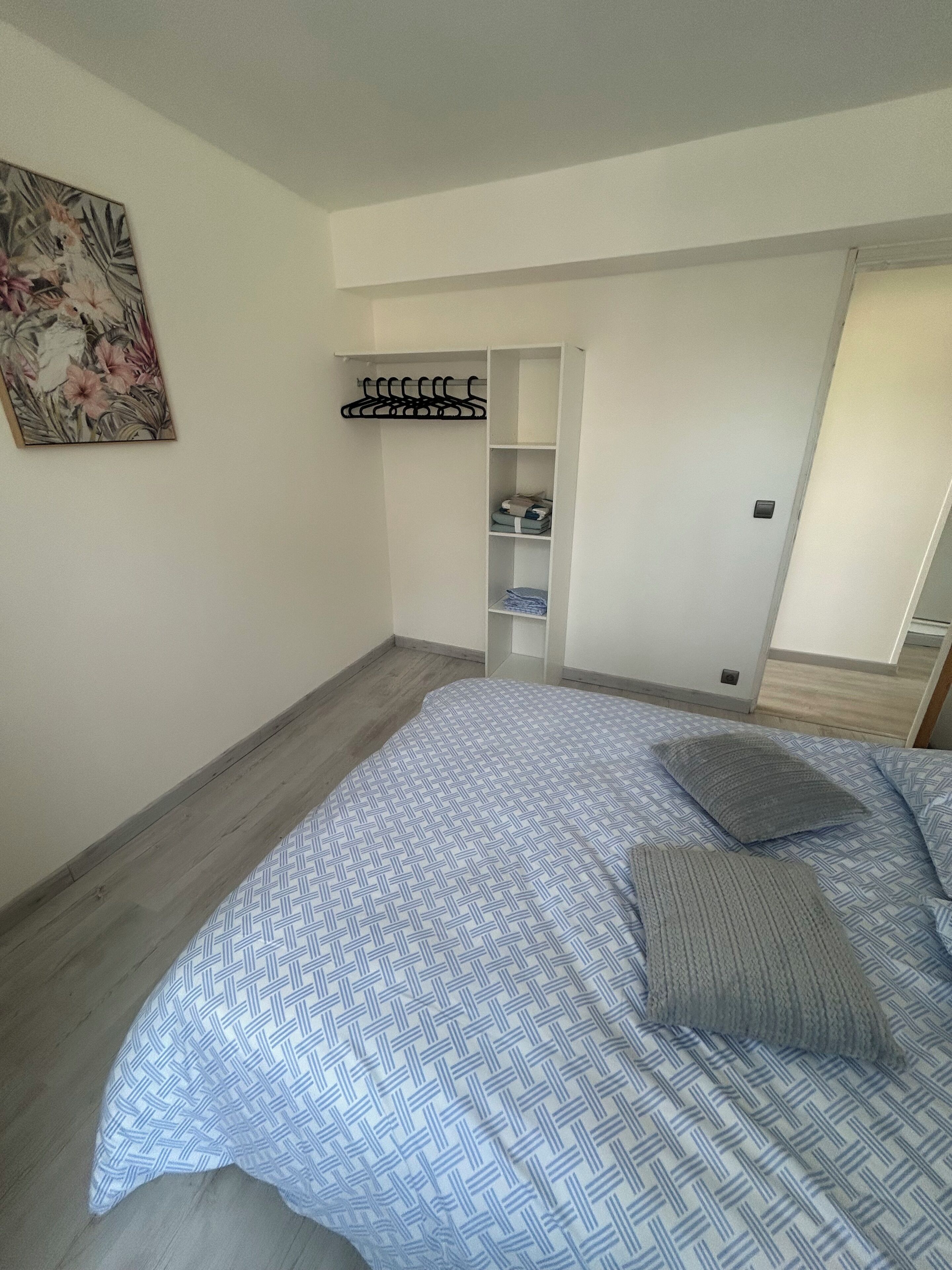 A bedroom with a bed, a hanging coat rack, and a door leading to another room.