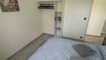 A bedroom with a bed, a hanging coat rack, and a door leading to another room.