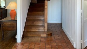 Uma escada com degraus de madeira e um corrimão branco, que leva a um quarto com uma luminária sobre uma mesa.