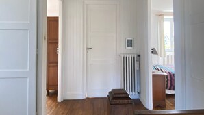 Um corredor com piso de madeira, paredes brancas e uma porta que dá para outro quarto.