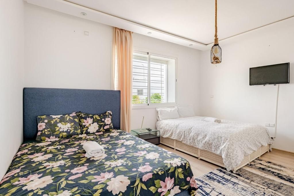 Une chambre avec un grand lit, un plus petit lit, une télévision et une fenêtre avec des rideaux.