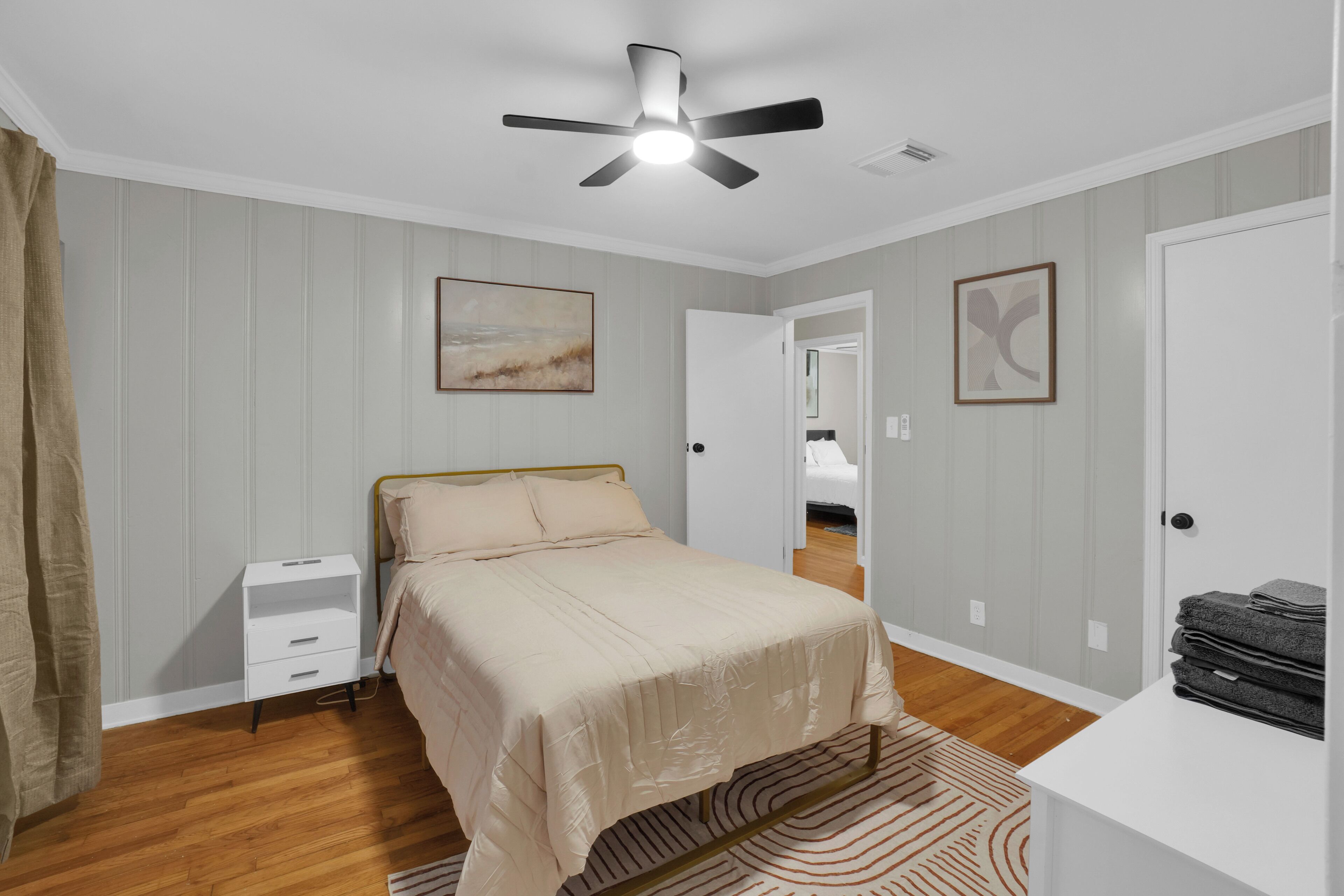 A bedroom with a bed, a nightstand, a ceiling fan, and a door leading to another room.