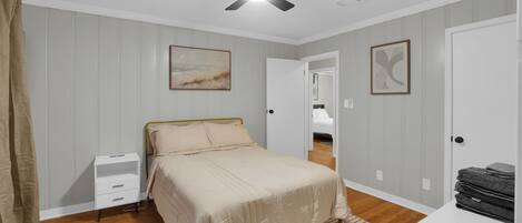 A bedroom with a bed, a nightstand, a ceiling fan, and a door leading to another room.