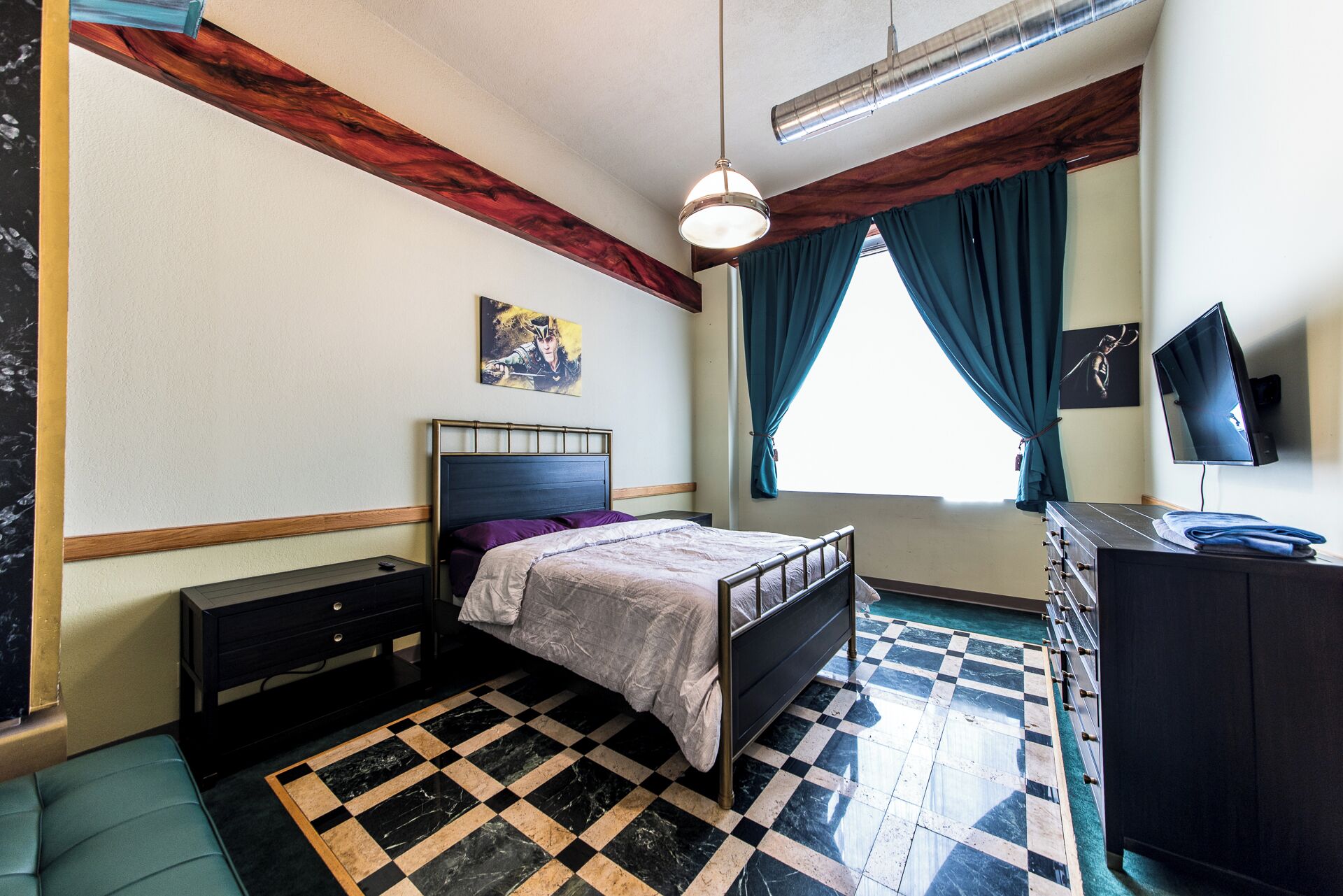 A bedroom with a bed, a dresser, a television, and a window with curtains.