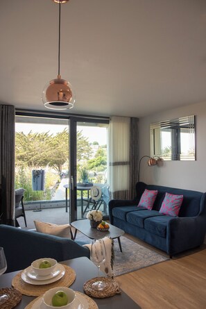 A modern living room with a sofa, coffee table, and dining area. - Liner Apartment 7 (Falmouth)