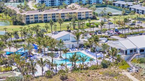 A resort with a swimming pool, palm trees, and multiple buildings. - Place in Paradise, Tropical 1 Bedroom with Golf Course in Ocean Village (Fort Pierce)