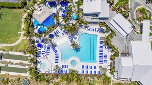 An aerial view of a resort with a central swimming pool, multiple lounge areas, and palm trees. - Place in Paradise, Tropical 1 Bedroom with Golf Course in Ocean Village (Fort Pierce)