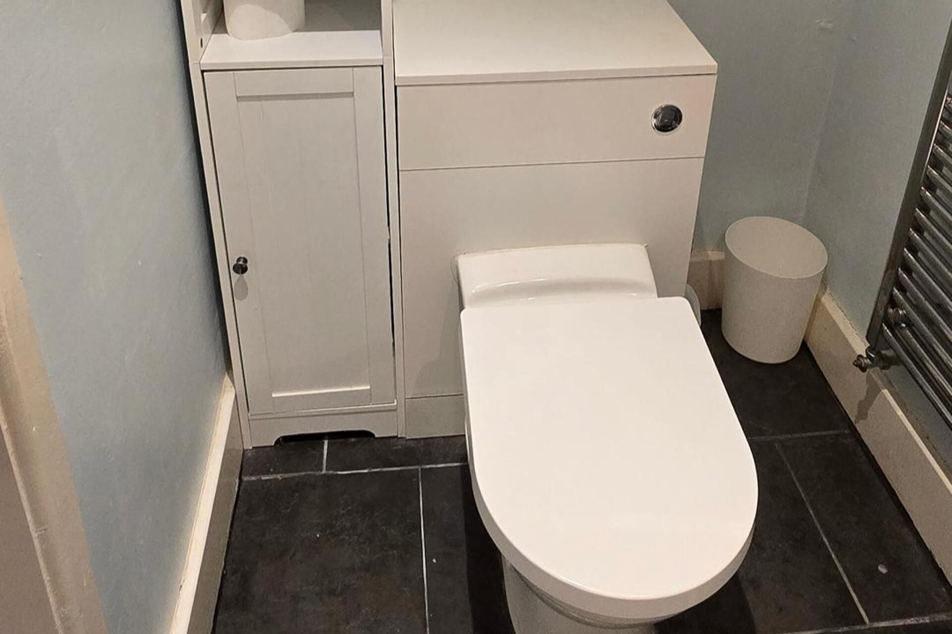 A bathroom with a toilet, a small cabinet, and a radiator.