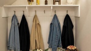 A hallway with a coat rack holding several jackets, a potted plant, a vase with flowers, and a wall-mounted lamp. - Luxe Haven Stays Spacious 3BR Near NRG, Med Center & Downtown Houston (Houston)