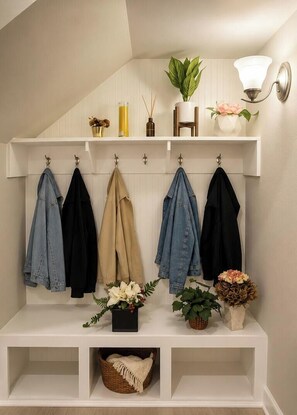 Eine Diele mit Kleiderhaken, an denen mehrere Jacken hängen, einem Blumentopf, einer Blumenvase und einer Wandleuchte.