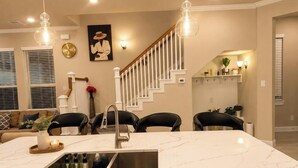 A modern kitchen with a marble countertop, a built-in sink, and a staircase with white railings. - Luxe Haven Stays Spacious 3BR Near NRG, Med Center & Downtown Houston (Houston)