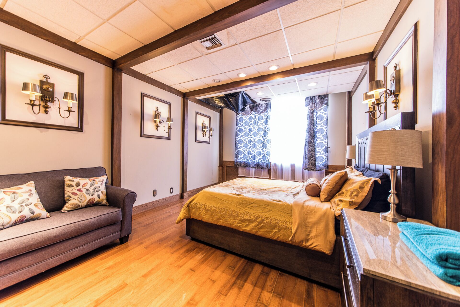 A bedroom with a bed, a sofa, a nightstand, and a window with patterned curtains.