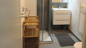 A modern bathroom with a glass shower enclosure, a wooden drying rack, a white sink with a mirror, and a toilet. - Two-bedroom apartment with a private garden, air conditioning, and two parking spaces. (Istres)