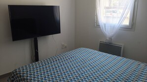 A bedroom with a bed, a television, an air conditioning unit, and a window with curtains. - Two-bedroom apartment with a private garden, air conditioning, and two parking spaces. (Istres)