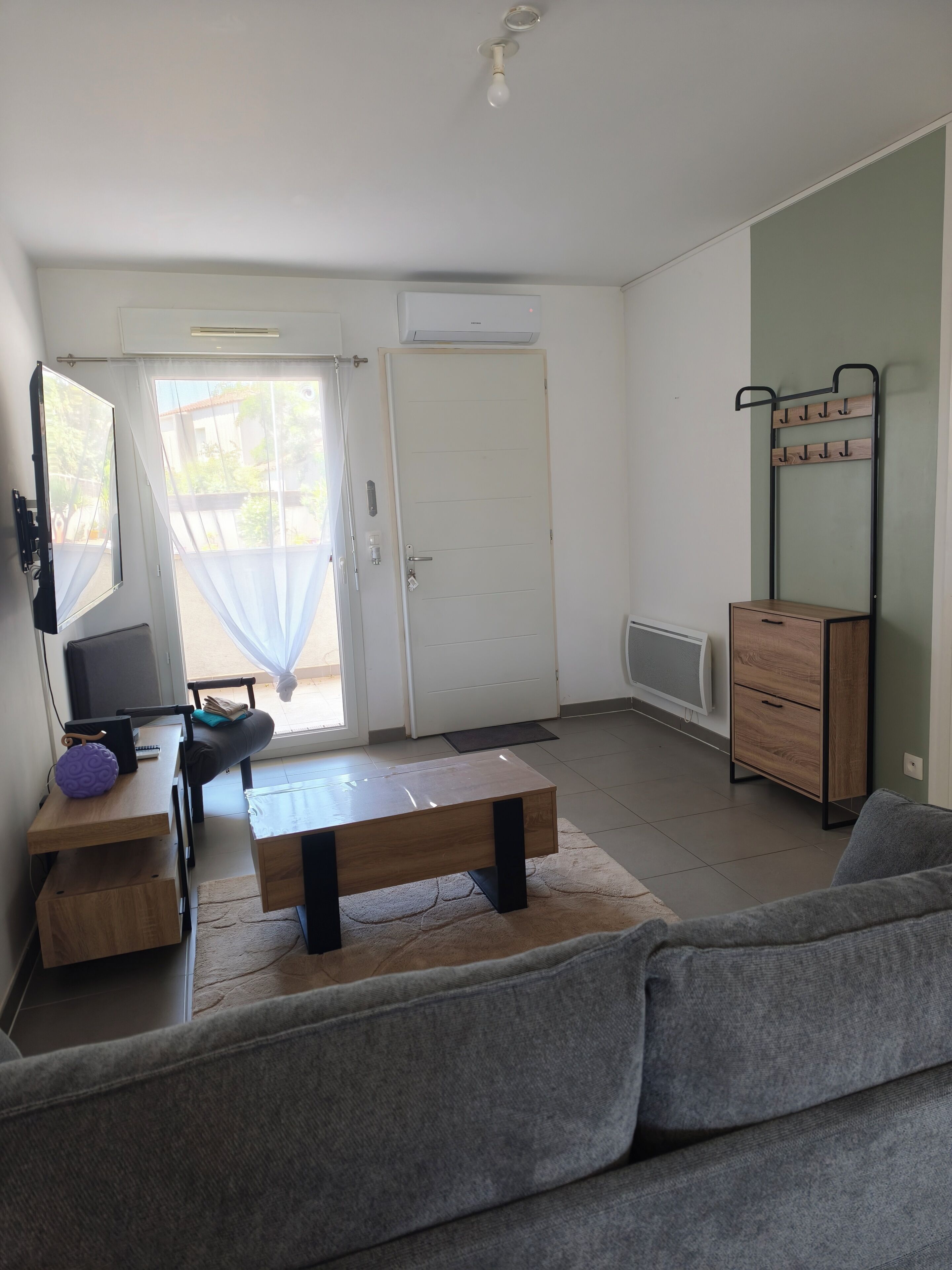 Un salon comprenant un canapé, une table basse, un téléviseur et une porte donnant sur un espace extérieur.