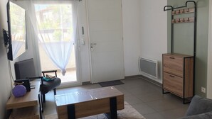 A living room with a sofa, a coffee table, a TV, and a door leading to an outdoor area. - Two-bedroom apartment with a private garden, air conditioning, and two parking spaces. (Istres)